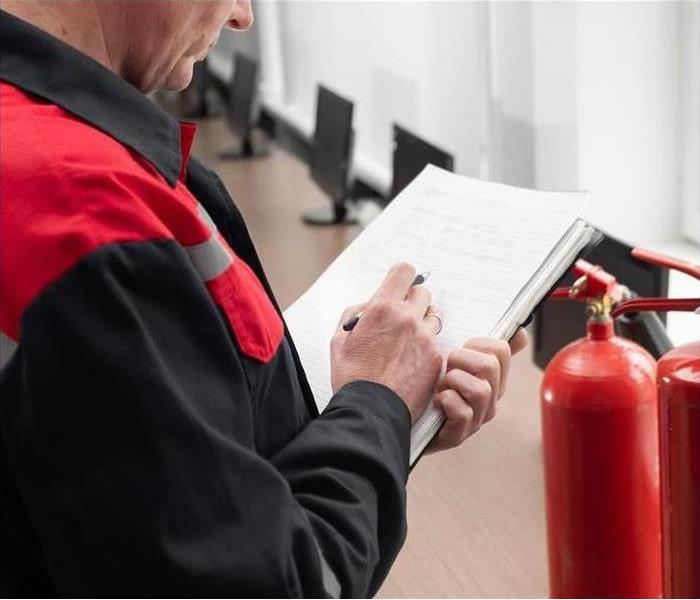 ?Man writing in notebook next to a fire extinguisher